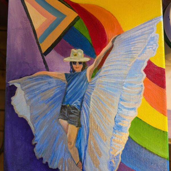 Oil painting shows a woman with large white wings standing in front of a large Pride flag. She appears to be dancing and lifts up the wings.