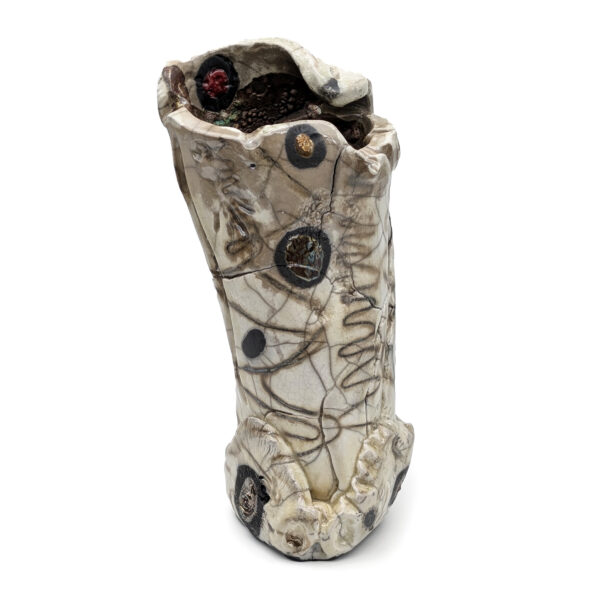 Round cylindrical sculpture with wavy edges. The sculpture is grayish-white, etched with lines, circles and scribbles.