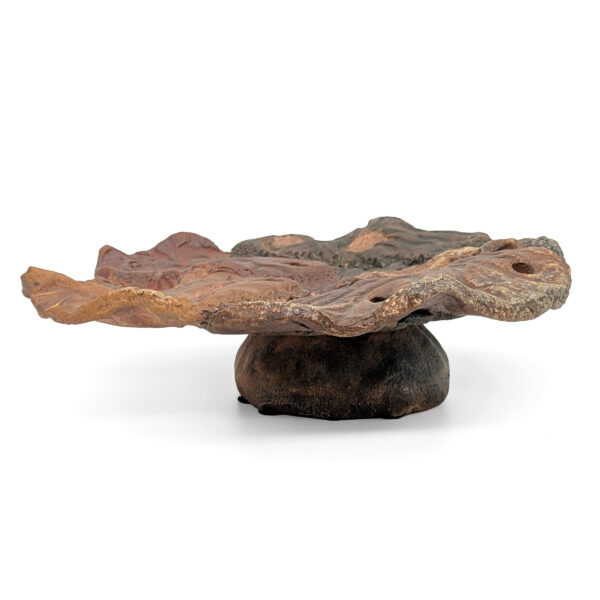 Abstract sculpture of a round platter with uneven edges on a stand. The sculpture is shades of earth brown, yellow and dark grayish-blue