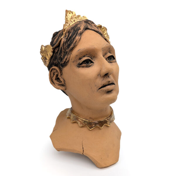 Ceramic bust of a female face, turned slightly to one side. The figure has brown hair and wears a gold crown and gold choker necklace.