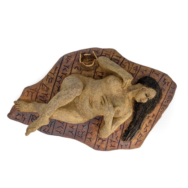 Ceramic sculpture of a nude figure lying on a brown base patterned with black script. She looks to one side with a contemplative expression.