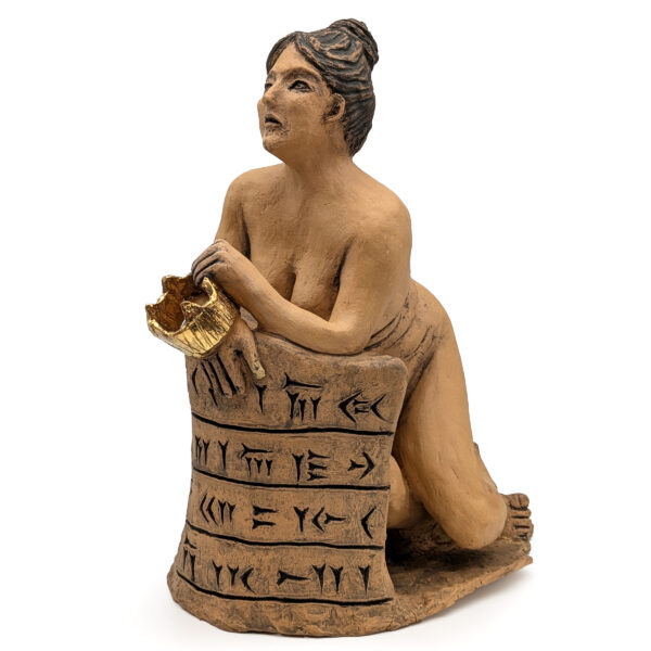 Ceramic sculpture of a nude woman leaning forward against a large ceramic wall. The wall has black script written in lines. The woman holds a gold crown in one hand.