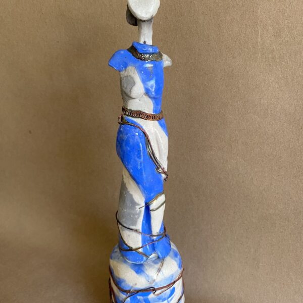 Ceramic sculpture of an elongated abstract female figure. The round head is featureless. The sculpture features waves of blue and white.