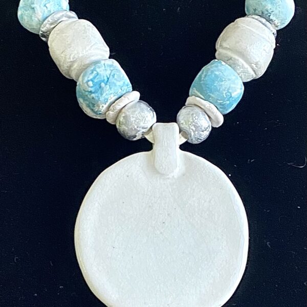 Necklace of large irregular round ceramic beads and a large flat circular pendant at the center. The beads alternate colors between light blue and white.