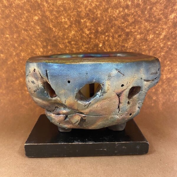 Round ceramic vessel in iridescent blue. There are holes throughout the piece.