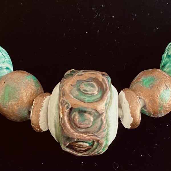 Necklace of large irregular round ceramic beads, with a large patterned bead at its center. The beads are multicolored tan, beige and green hues.