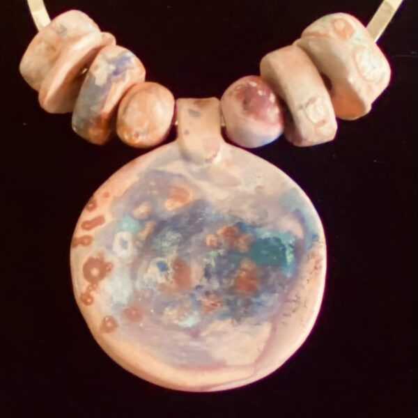 Necklace of large irregular ceramic beads and a large flat circular pendant in the center. The beads are multicolored tan, beige, brown, blue and pink hues.