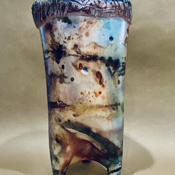 Round iridescent vessel on ceramic feet. The sculpture has a round ridged edge around the top.