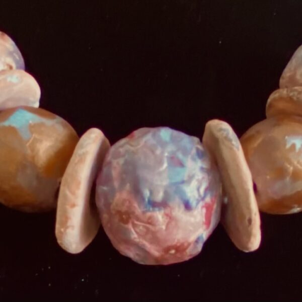 Necklace of large round ceramic beads alternating with flat circular ceramic beads. The beads are multicolored tan, beige, brown, blue and pink hues.