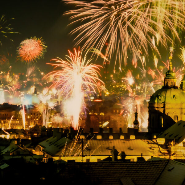 Photograph shows fireworks exploding against a dark night sky over buildings and rivers. The fireworks are shades of gold, illuminating the city below.