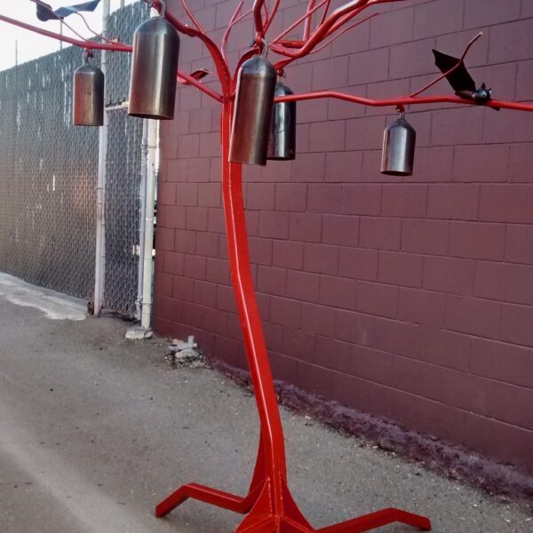 Photgraph shows a red metal sculpture of a tree. Large metal objects and bats hang in its branches.