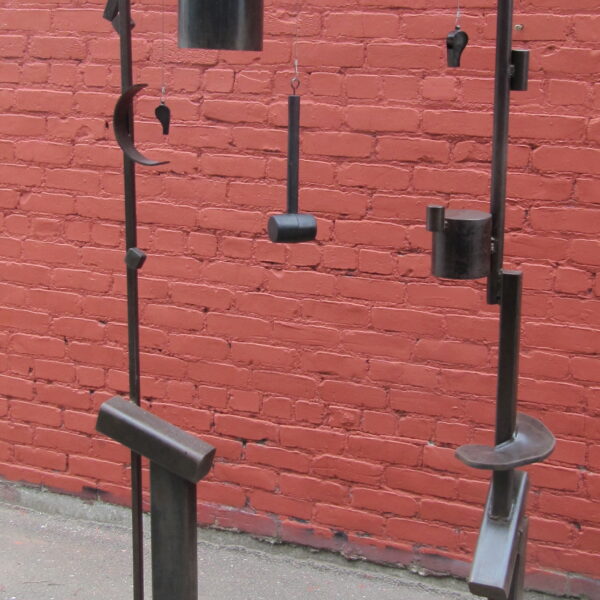 Photograph shows a large metal sculpture with bells hanging from a structure.