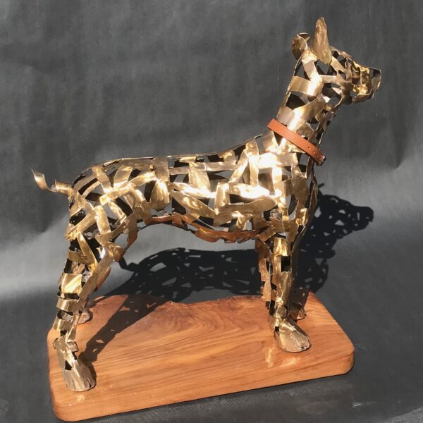 Photograph showing bronze sculpture of a dog on a wooden pedestal. The dog is made of bronze strips, with holes showing between.