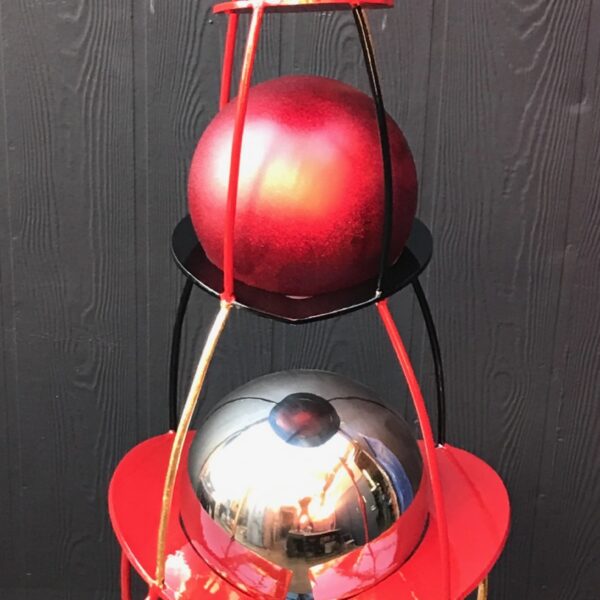 Photograph showing red metal sculpture. The sculpture has several stacked abstract shapes.