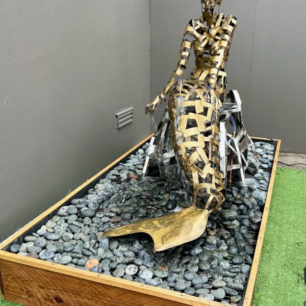 Photograph showing a bronze sculpture of a mermaid sitting on a bed of gravel.