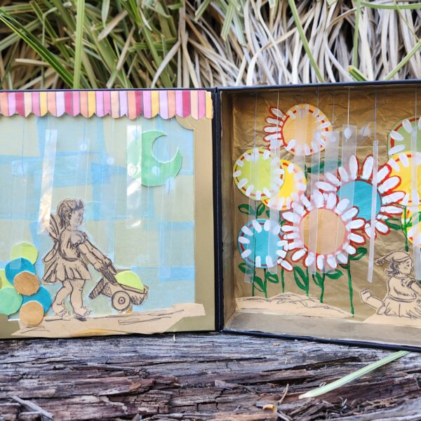 Photo shows open diorama adorned with paper flower designs. A figure is visible pushing a wheelbarrow.